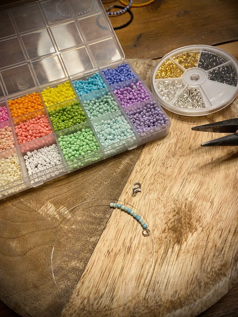 Großes Perlensortiment Bunte Perlen in einer Box, Werkzeuge und ein Holzbrett im Hintergrund.
