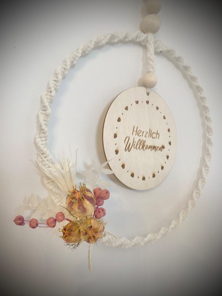 Makramee-Kranz Ein hängender Kranz aus Seil mit einer Holzscheibe und getrockneten Blumen.